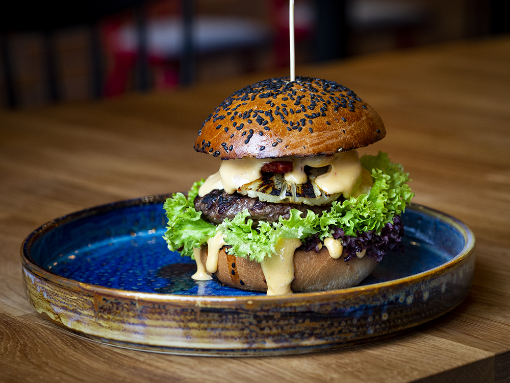 Na zdjęciu widać burgera na niebieskim, eleganckim talerzu.