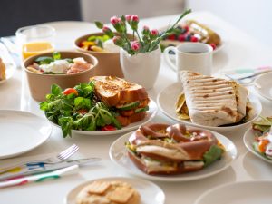 Na zdjęciu widać śniadanie ustawione na stole. Białe talerze i dania: chałkę, precel i tortillę.