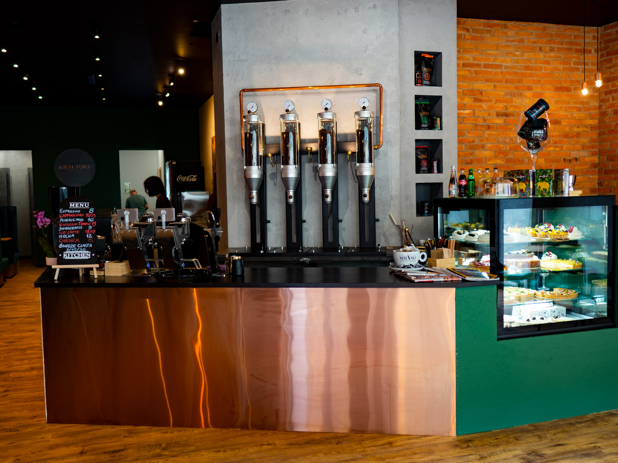 Zdjęcie przedstawia wnętrze kawiarni Kraftowa - bar, witrynę z deserami i salę.